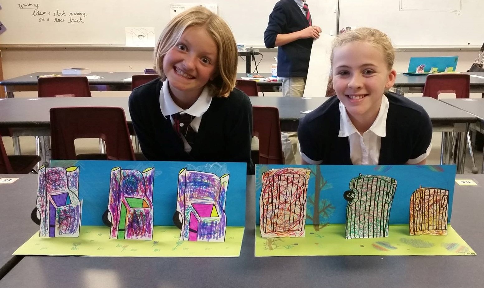 Two elementary students smiling while holding their finished art projects