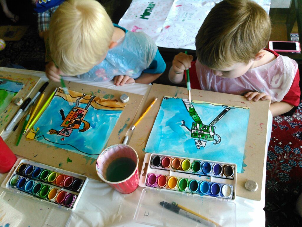 Overhead view of children painting with watercolor supplies on a classroom table